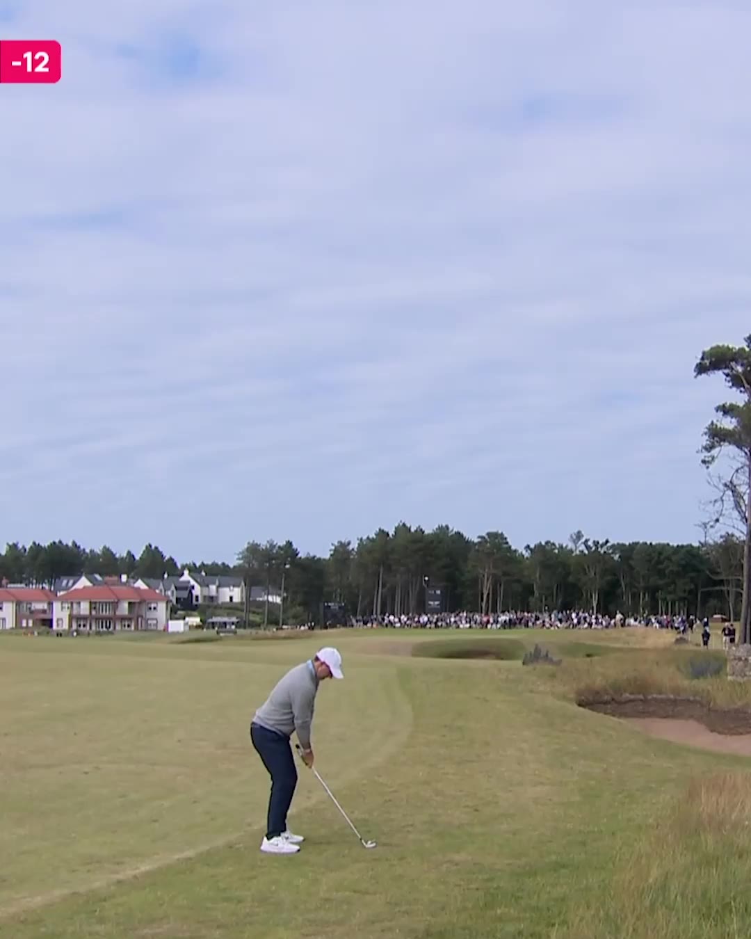 A golfer in gray sweater and dark trousers hits a tee shot that curves sharply, with an on-screen ball-speed graphic reading 142mph and a scoreboard tag of -12; later frames show a shaky, blurred pan across sky and rough with spectators walking a dirt path.