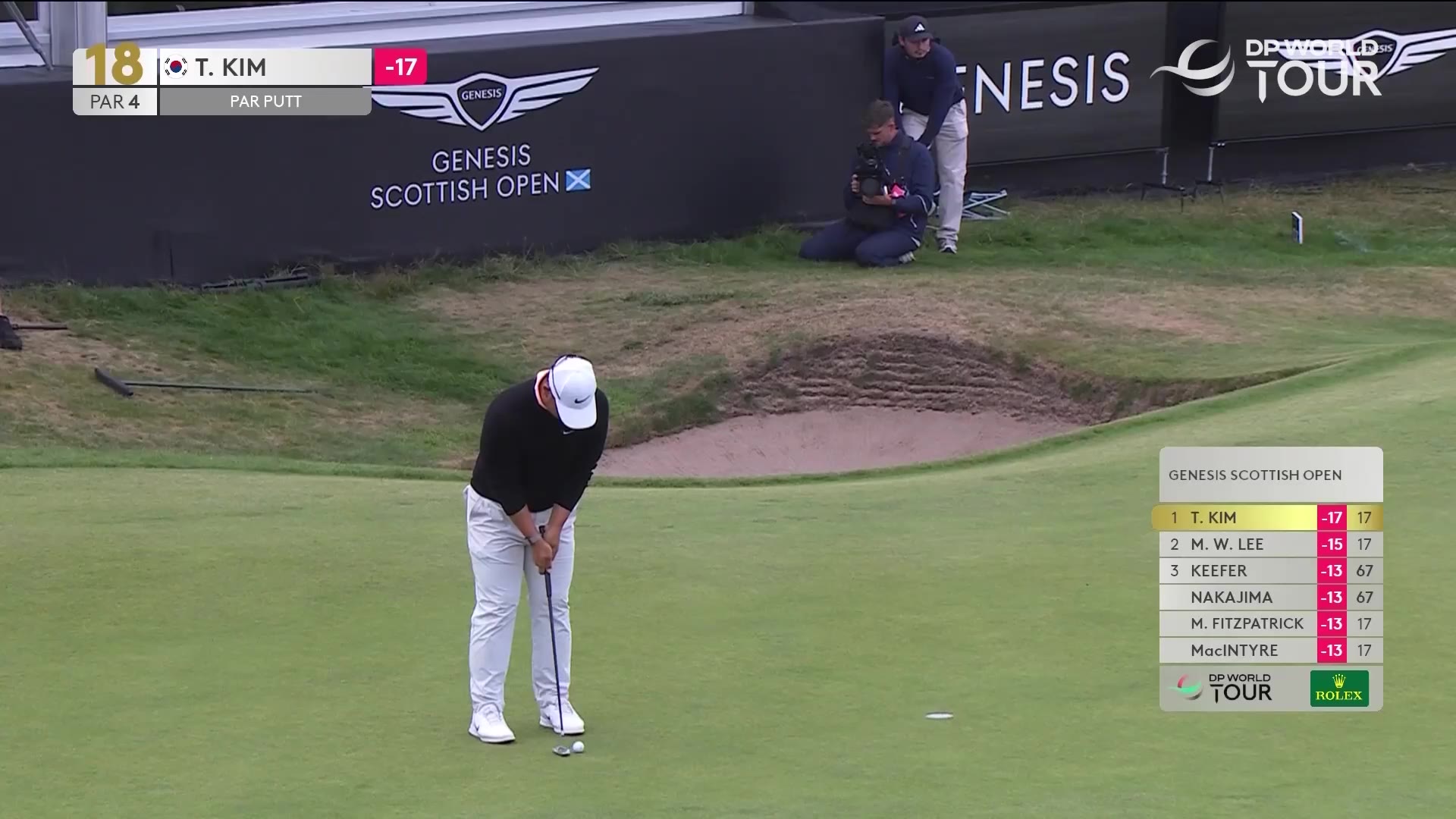 Golfer Tom Kim on the 18th hole green in front of a large grandstand crowd, followed by a close-up of him bowing his head with sunglasses on his cap; on-screen graphic reads GENESIS SCOTTISH OPEN leaderboard: 1 T. KIM -17 64, 2 M.W. LEE -15 17, 3 KEEFER -13 67, NAKAJIMA -13 17, M. FITZPATRICK -13 17, MacINTYRE -13 17, with DP World Tour logo.
