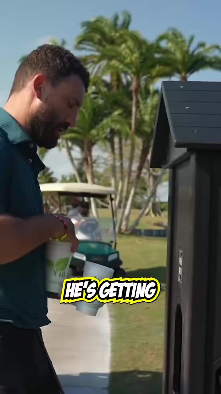 A bearded man in a teal striped golf polo picks up cups from a beverage station near a golf cart on a course lined with palm trees, then hands cups to someone off-screen; a different man in a navy polo and light blue shorts walks away carrying a golf club and holding a cup.
