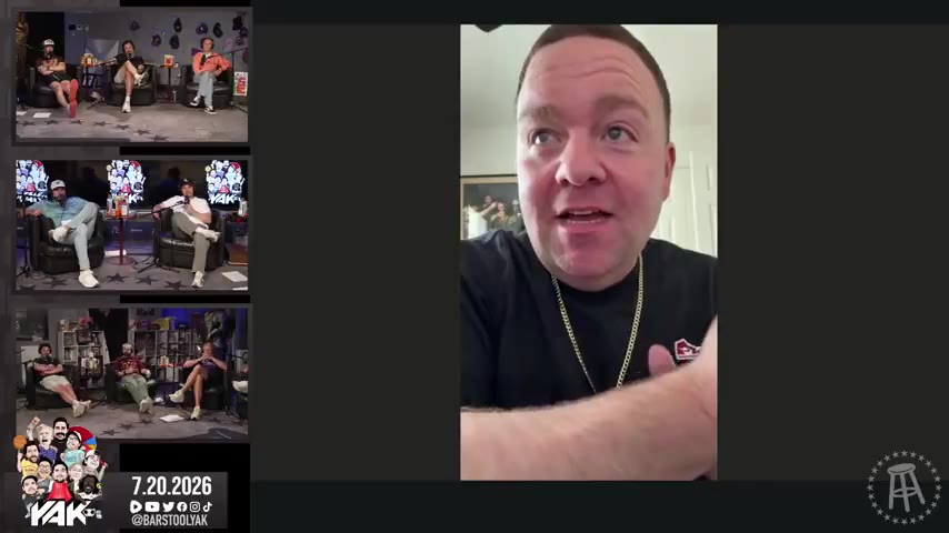A man with short brown hair wearing a black t-shirt and a gold chain with a cross pendant speaks directly to the camera in what appears to be a video call or selfie-style recording, set against a home interior background with a framed picture visible; a filmstrip of other people seated in chairs on a stage appears on the left side of the frame.