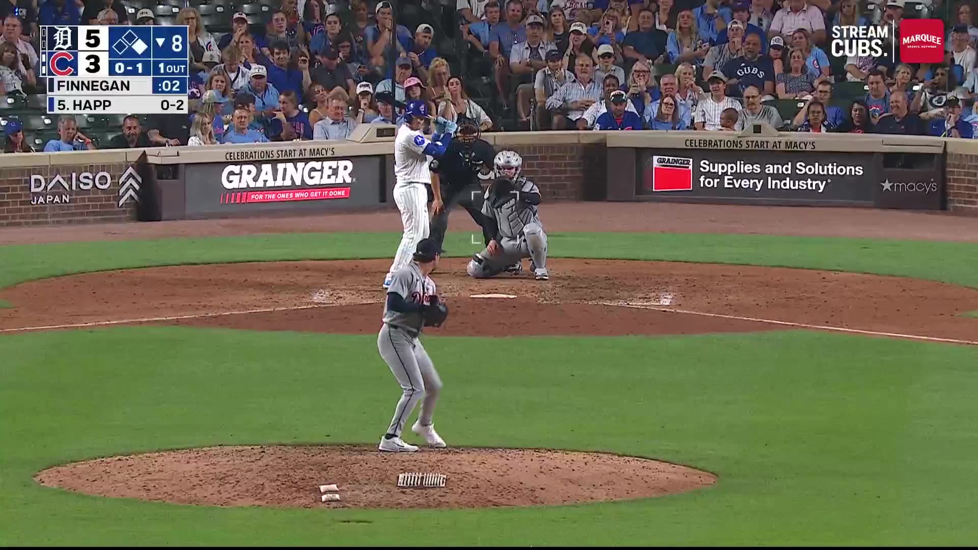 Ian Happ batting at Wrigley Field, Cubs trailing the Tigers 5-3 in the bottom of the 8th with one out; the batter drives a pitch and fans in the outfield seats jump up celebrating as a ball lands in the bleacher crowd.