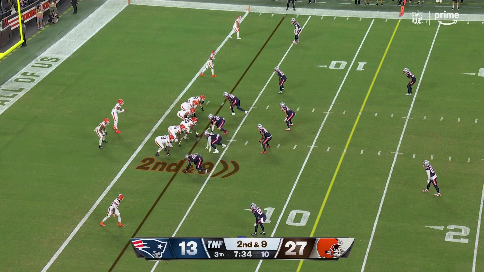 A New England Patriots defender intercepts a pass and returns it, with Cleveland Browns players nearby; scoreboard shows Patriots 13, Browns 27, 2nd & 9 in the 3rd quarter.