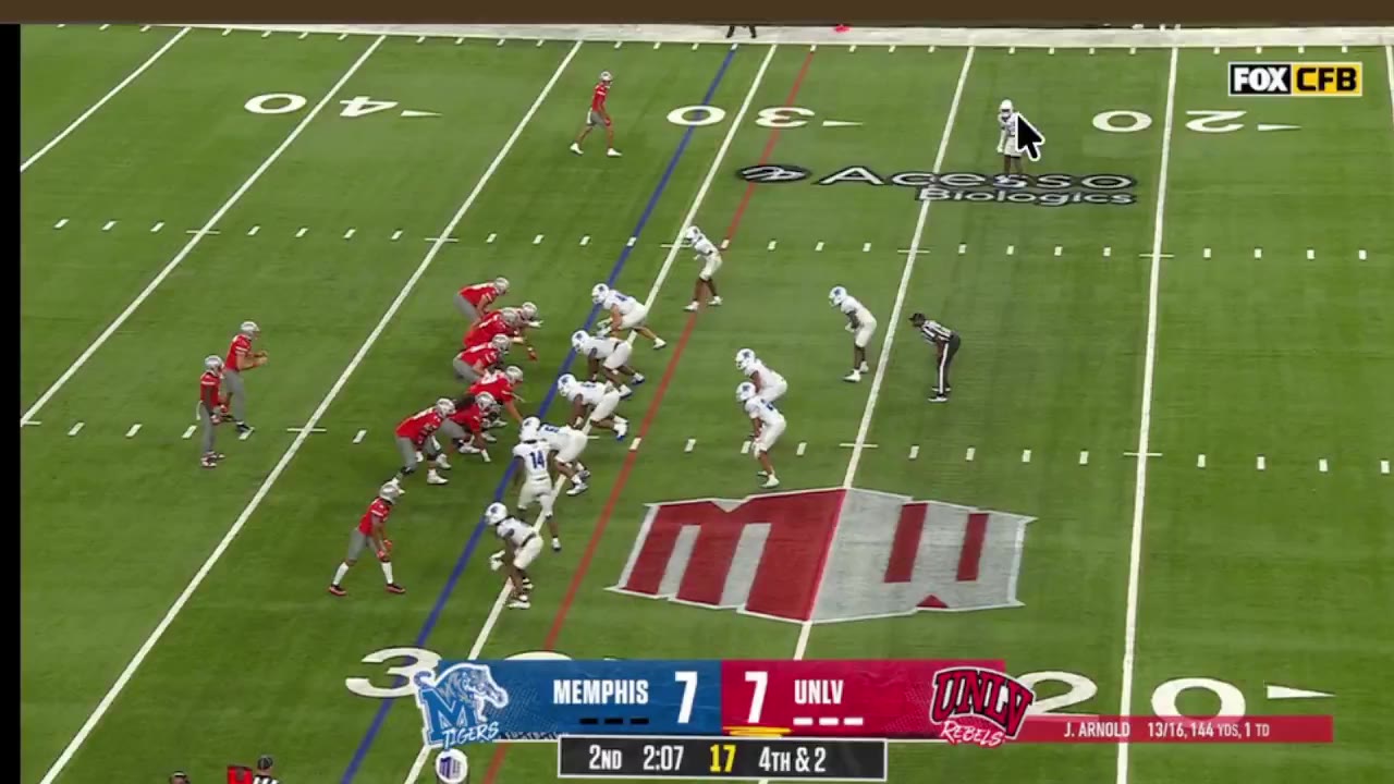 A running back cuts through the offensive line and breaks into the open field for a long touchdown run, with Memphis and UNLV players on the field and the scoreboard reading Memphis 7, UNLV 7, 4th & 2, then celebrates with a teammate afterward.