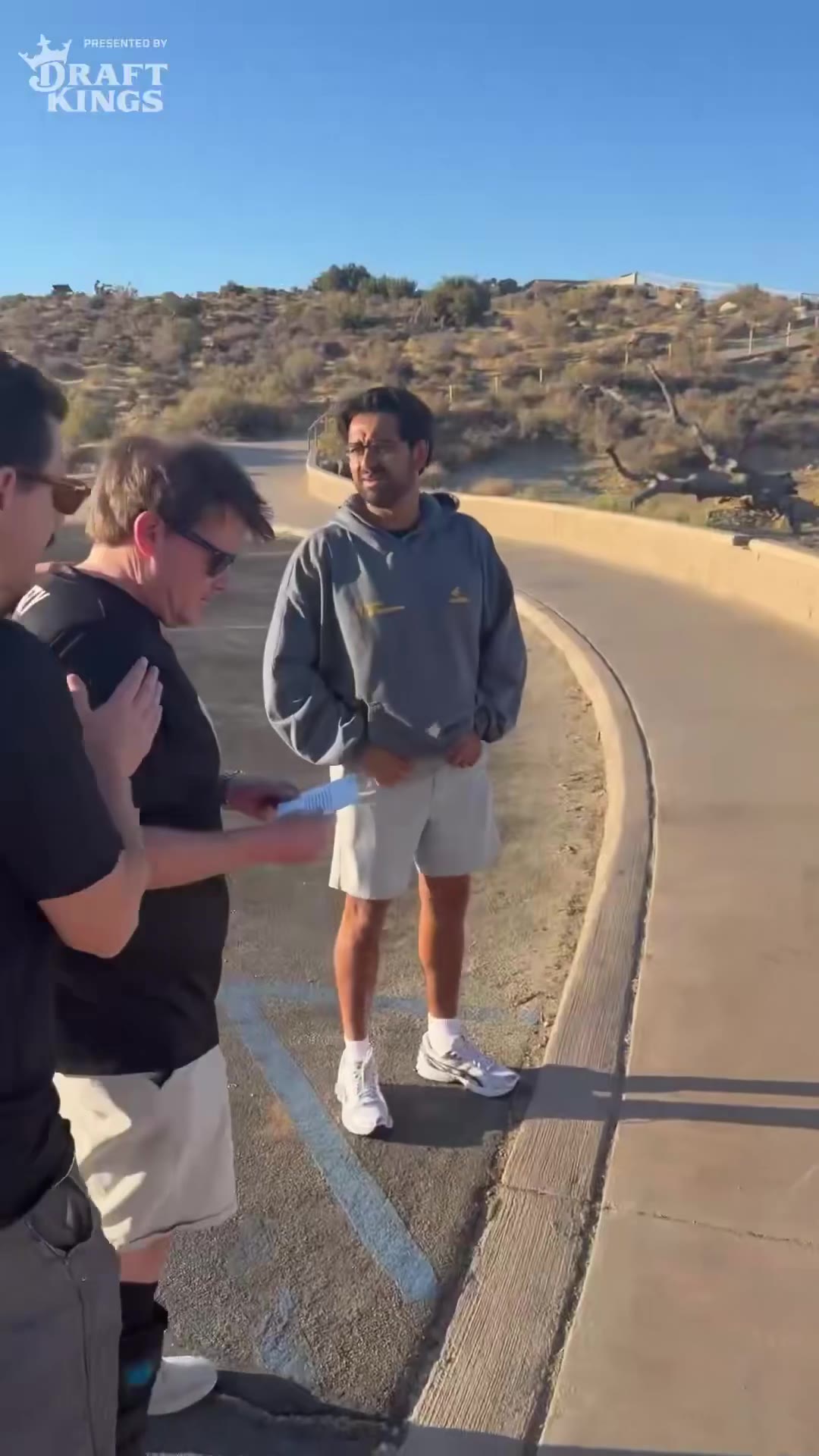 A person on inline skates loses balance while leaning on a wooden handrail along a paved desert trail, then in a later shot walks the same railed path on crutches with one leg in a medical boot, wearing a helmet and protective pads.
