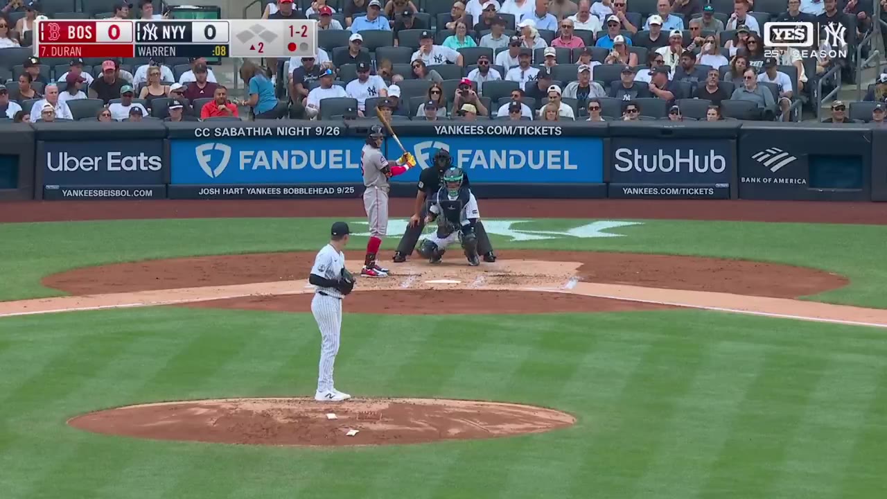 A Yankees infielder in a black cap turns and throws the ball while balanced on one leg, with a Red Sox baserunner in a gray uniform running along the baseline near a bag as an umpire watches; scoreboard shows Red Sox 0, Yankees 0.