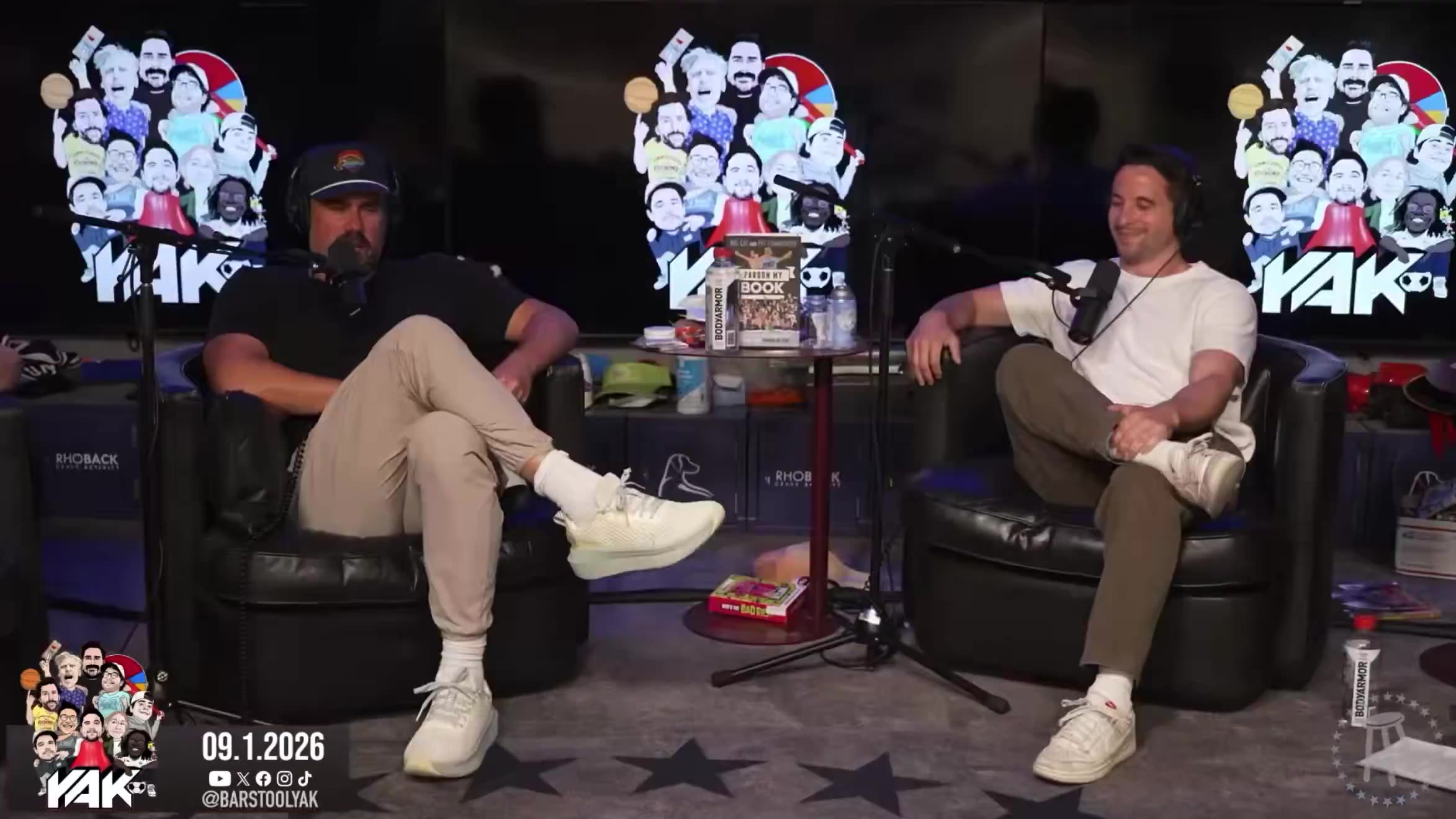 Two men sit in podcast studio chairs across from each other, one wearing a headset and khaki pants gesturing with his hands; a wider shot then shows three men seated in a podcast studio with sports memorabilia shelving behind them, one in a red Ohio State sweatshirt, one in light clothing with a trucker hat, and one in a dark shirt with his arm raised behind his head.