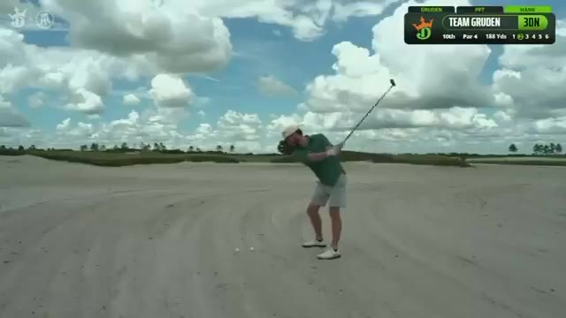 A golf shot flies in a long arc over sand dunes toward a green, with the player watching from a sandy fairway area; on-screen graphics show a golf broadcast overlay reading TEAM GRUDEN, 3 DN, hole 10, Par 4, 188 Yds.