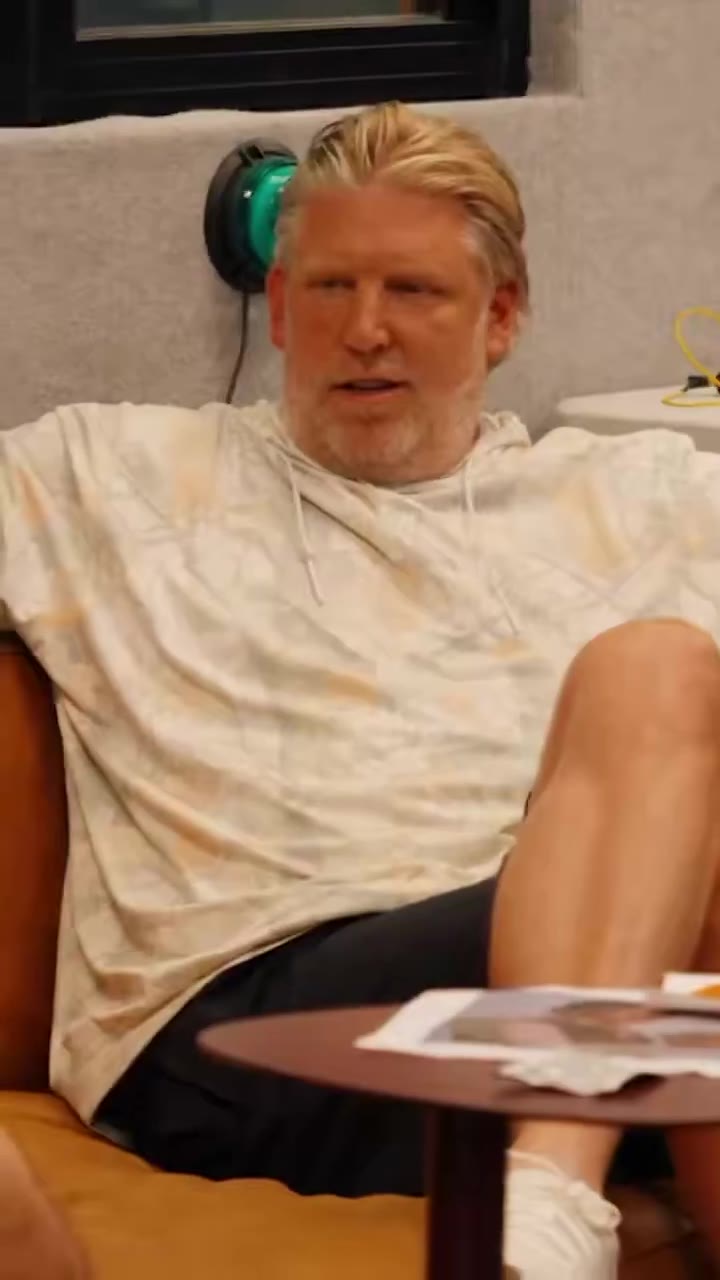 Multiple men are seated on orange leather couches in a lounge/bar setting with a DraftKings sportsbook sign visible; a bearded man in a white cap and NOBULL shirt is speaking animatedly and gesturing toward others off-frame.