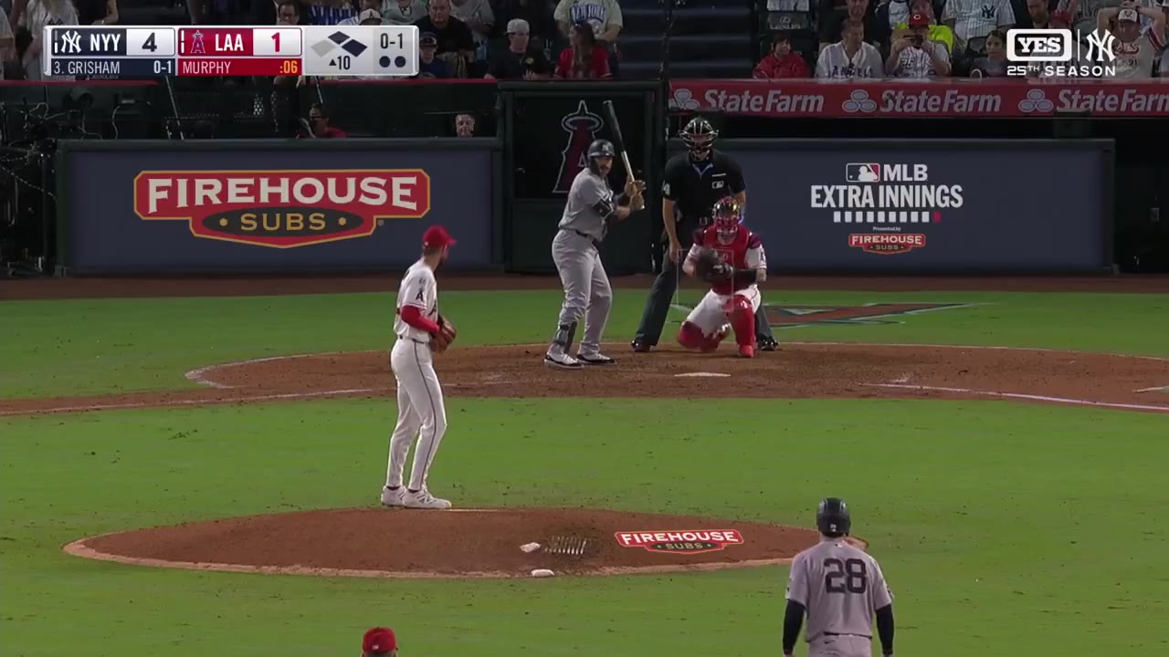 A New York Yankees baserunner scores and is greeted at home plate, with the on-screen scoreboard showing Yankees 5, Angels 1 during an Angels-Yankees game.