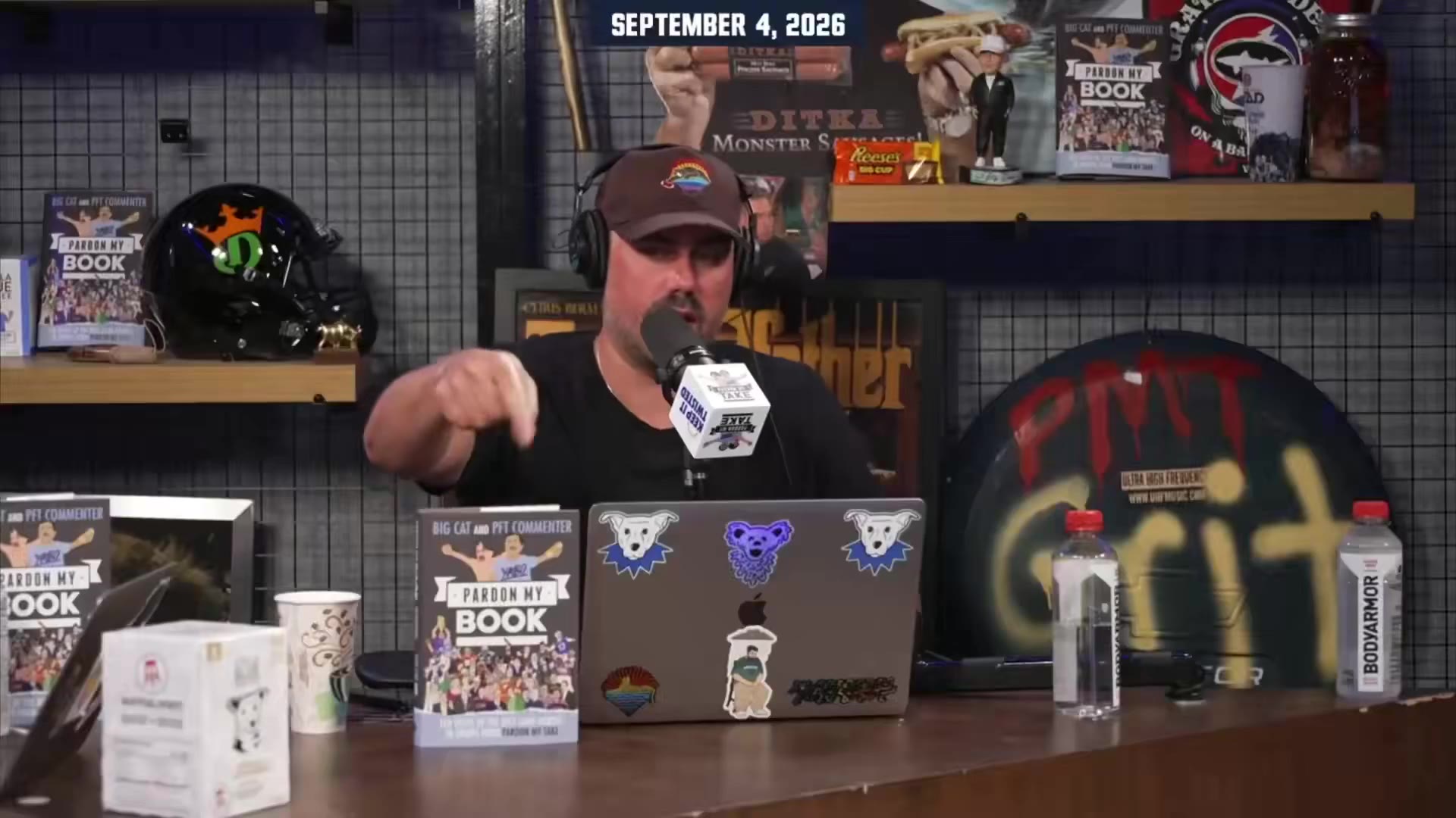 Two men sit on a podcast set; one man in a Baltimore Ravens t-shirt and backwards cap sits on a leather couch talking and gesturing animatedly, the other with a mustache and headset sits at a desk speaking into a microphone in front of a laptop with sticker decals, a TickPick-branded screen on the wall behind the couch, dated September 4, 2026.